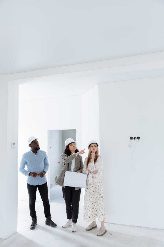 Real estate agents and clients discussing property plans indoors wearing hard hats.